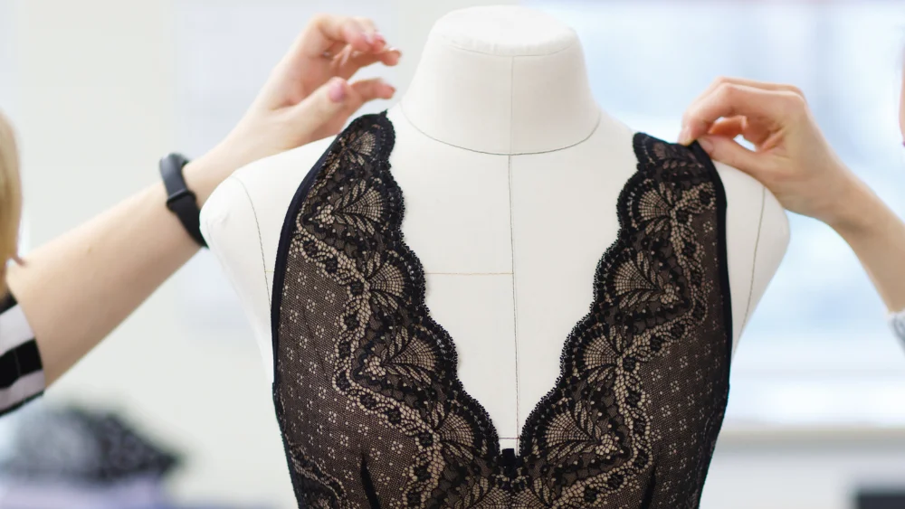 Lingerie Manufacturer’s Production Capacity in Design and Prototyping - Supreme Lingerie A designer adjusting black lace lingerie on a mannequin, demonstrating a lingerie manufacturer’s production capacity in design and development.